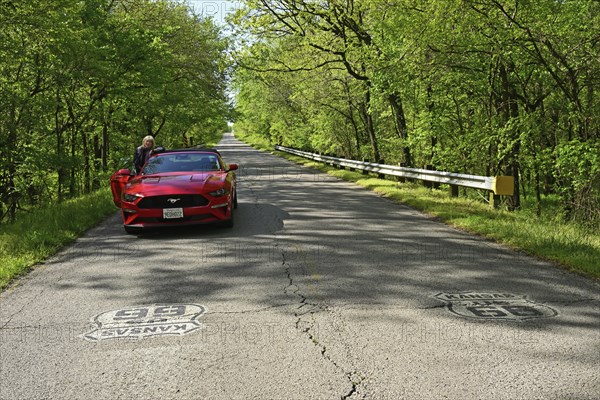 Red Ford Mustang parked on historic Route 66 in the middle of a forest in Kansas