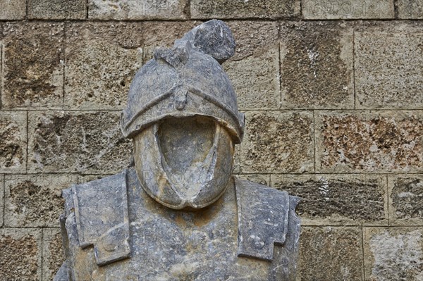 Stone figure of a headless knight in armour in front of a rustic wall, outdoor area, Archaeological