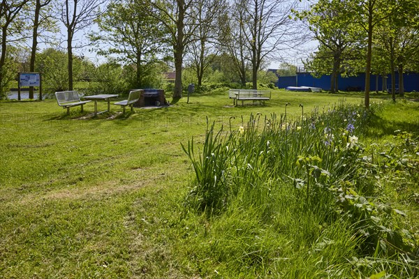 Small park with flowers, lawn and a public barbecue area with brick barbecue, benches and tables in
