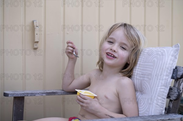 Boy, 5 years, blonde, sitting in garden chair, garden, eating pudding, yoghurt, enjoying, summer,