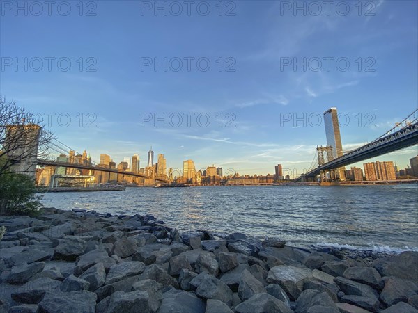 Manhattan skyline with bridges over the river at sunset seen from the shore, historic bridge in the