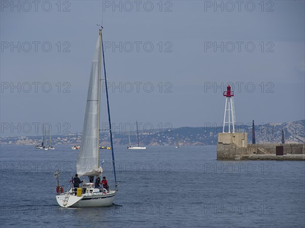 Sailing boat on the open sea, in the background more boats and a lighthouse, Marseille on the