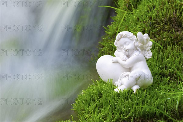 Porcelain angel figurine on moss by a waterfall