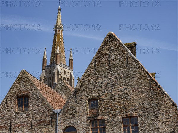 Old brick buildings with gothic tower in the background under a bright blue sky, historic city on
