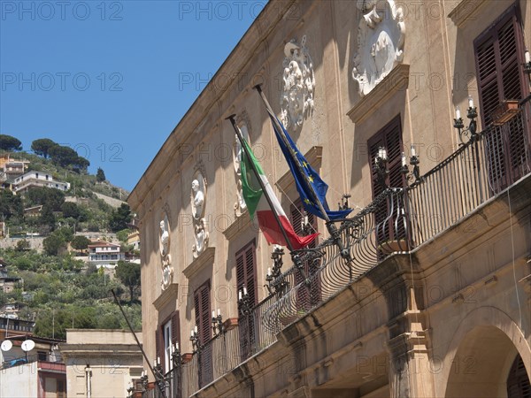 Building with italian and european flag on a balustrade in front of a sunny hillside, palermo in