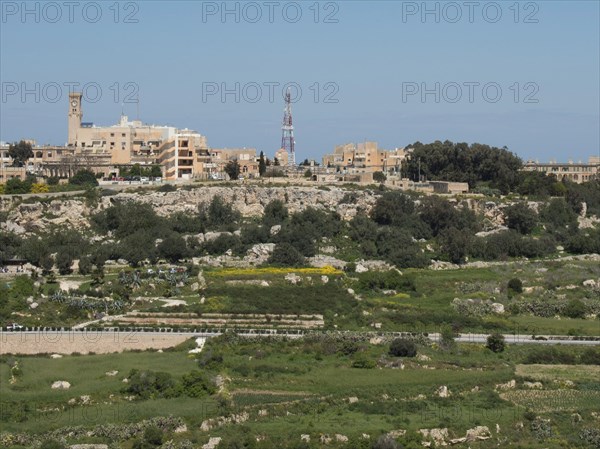 Overview of a town with various buildings, green areas and a striking tower in the background, the