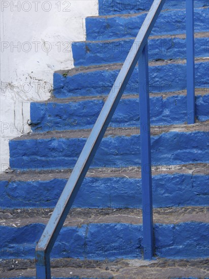 Close-up of a blue stone staircase with metal railing and white background, The volcanic island of