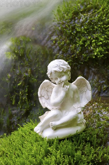 Porcelain angel figurine on moss by a waterfall