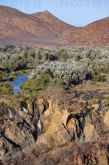Kunene River with green vegetation in dry red mountain landscape, waterfall and African Baobab
