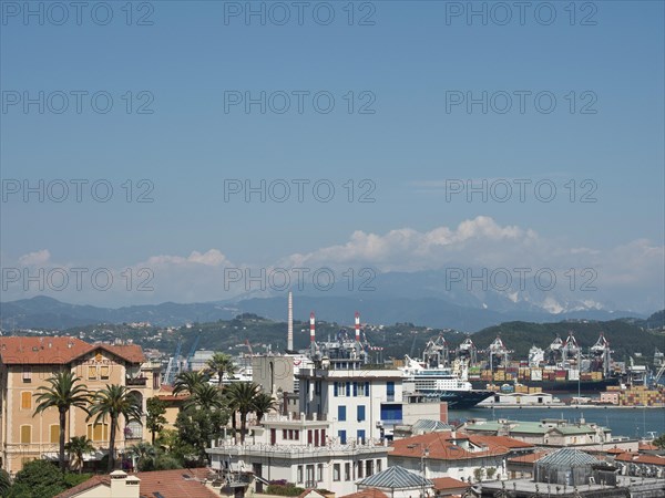 Panoramic view of a city with harbour, mountains and industrial buildings in the background under a