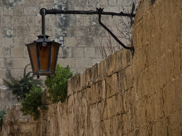 Old lantern on a traditional stone wall with some vegetation, the village of mdina on the island of