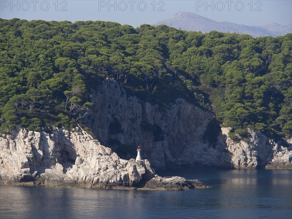 Small lighthouse on a rocky coast, surrounded by green trees and blue sea, the old town of