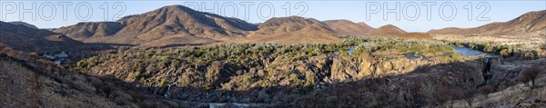 Panorama, Kunene River with green vegetation in dry red mountain landscape, waterfall and African