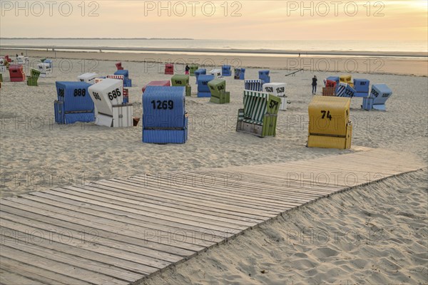 Colourful beach chairs on the sandy beach at sunset, a wooden path leads through the sand, summer