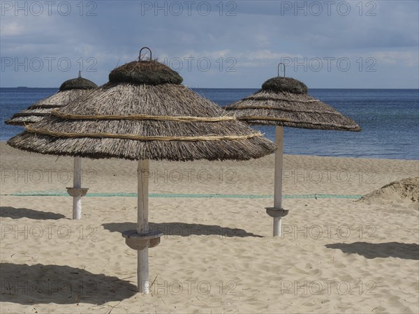 Beach with several thatched umbrellas and calm sea under partly cloudy sky, spring on the Polish