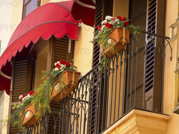Decorative balcony with red awnings, flower pots and plants standing in front of windows of a