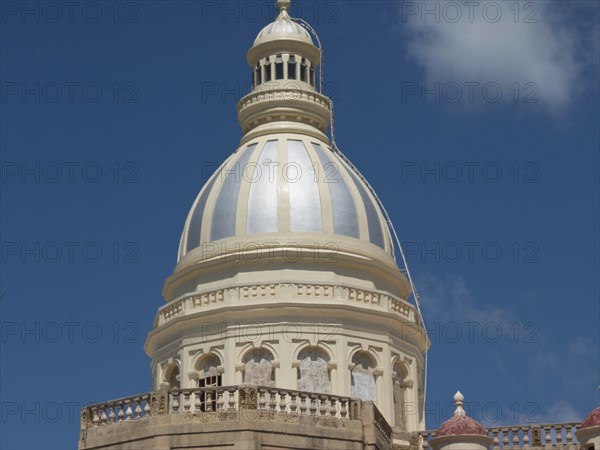 Large white-bluish dome of a religious building against a blue sky with some clouds, the island of