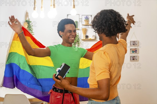 Gay male latin young friends taking photos raising LGBT flag at home