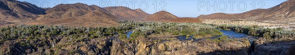 Panorama, Kunene River with green vegetation in dry red mountain landscape, waterfall and African