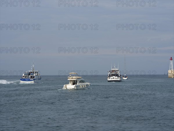 Boats sailing on the sea towards a harbour, accompanied by the wide sky and a lighthouse in the