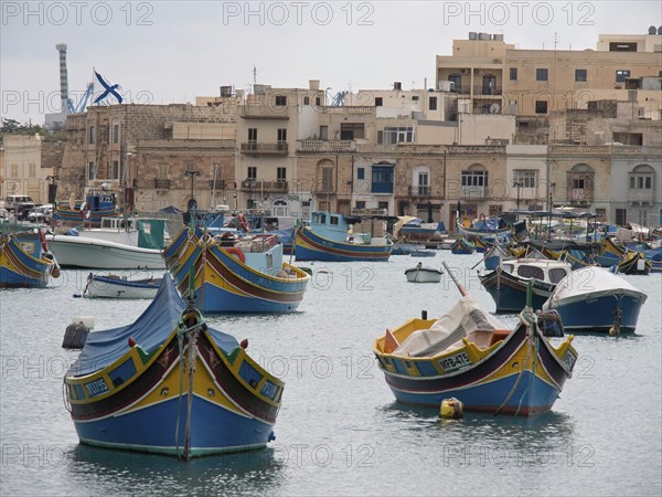 Several colourful boats in the harbour, behind them a town with many residential buildings and calm