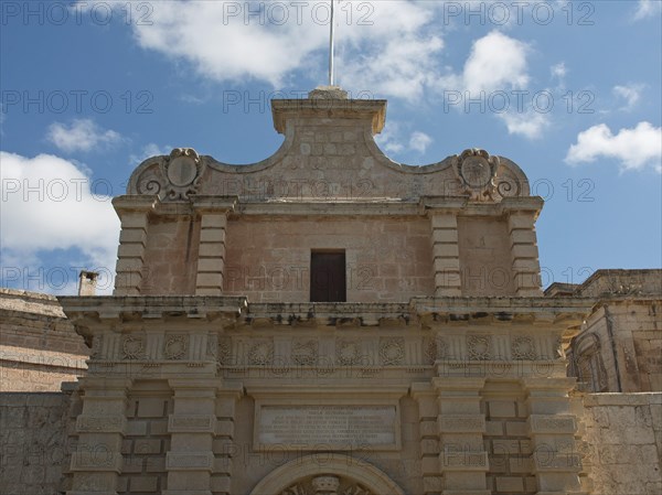 Entrance of a historic building with decorated stone archway under blue sky with clouds, the town