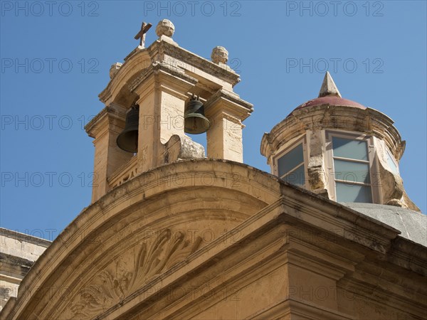 A building of an old church with bells and round windows under a blue sky, the town of mdina on the