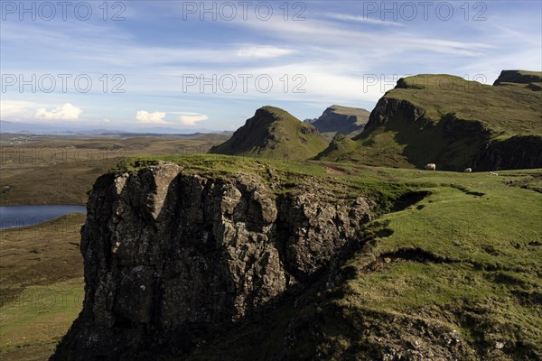 Dramatic cliffs and green slopes in an expansive mountain landscape under a blue sky with scattered
