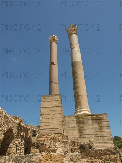 Two tall ancient columns rise into the blue sky, surrounded by ancient ruins, Tunis in Africa with