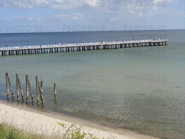 A long jetty leads into the calm sea under a cloudy sky on a sandy beach, spring on the Baltic