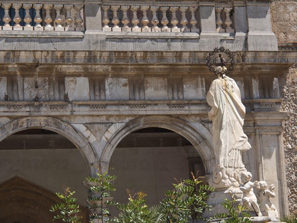 Marble sculpture of a figure and two angels in front of a church with arches and ornate details,