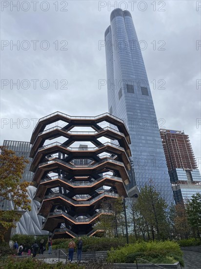 Modern building with unique architecture and skyscraper in the background on a cloudy day, people