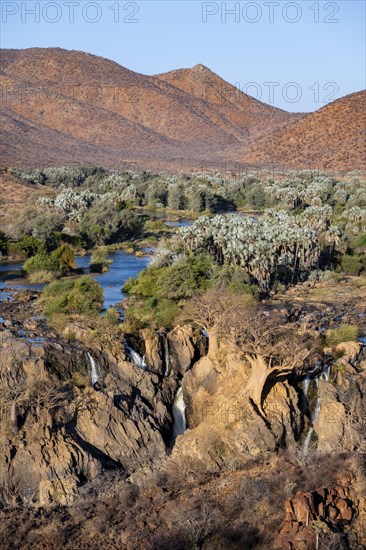 Kunene River with green vegetation in dry red mountain landscape, waterfall and African Baobab