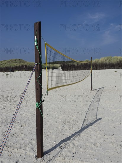 A volleyball net is set up in the sand on the beach, surrounded by dunes and grass, Heligoland,