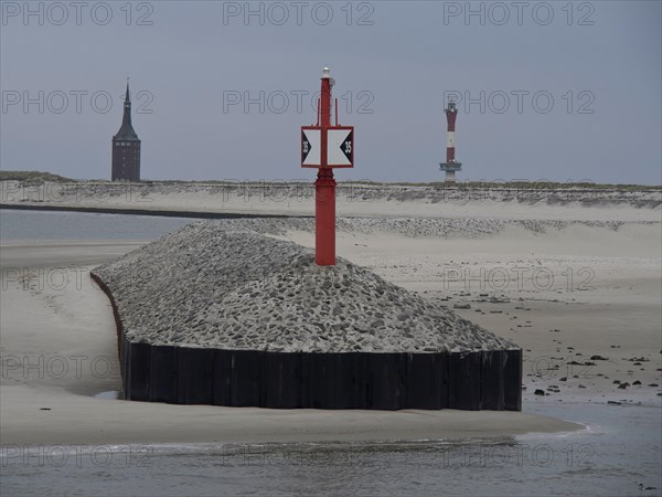 Red beacon on gravel embankment, church tower and lighthouse in the background, sand dunes and grey