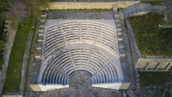 Aerial view of an ancient amphitheatre with stone seating steps surrounded by green areas,
