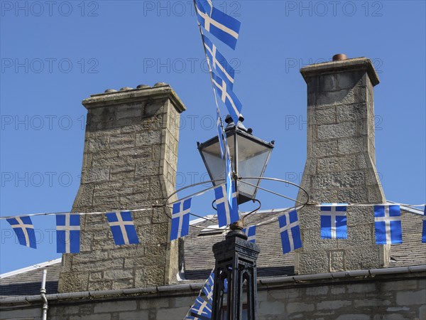 Stone houses in the village, decorated with blue and white flags and an old street lamp, grey