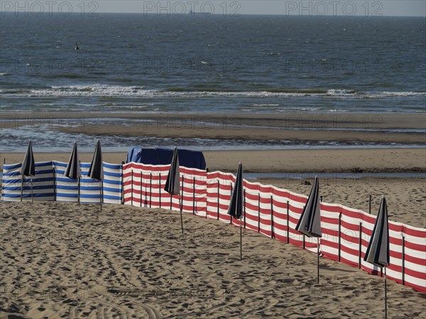 Wide sandy beach area with scattered blue and white striped and black umbrellas and the sea with