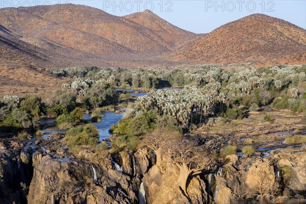 Kunene River with green vegetation in dry red mountain landscape, waterfall and African Baobab