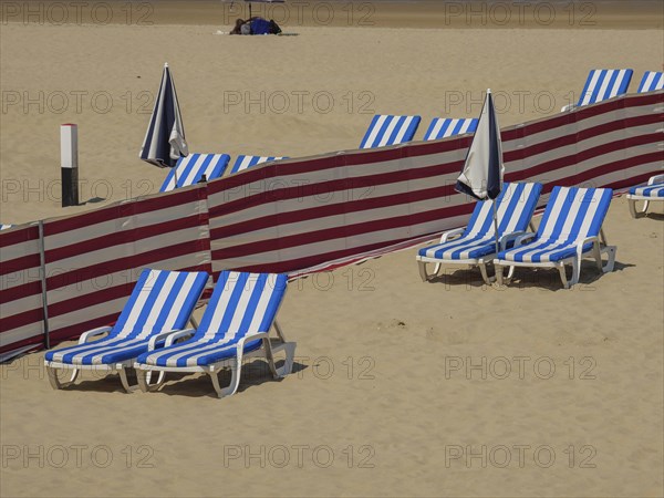 Beach where blue and white striped deckchairs, parasols and red partitions are arranged in rows,