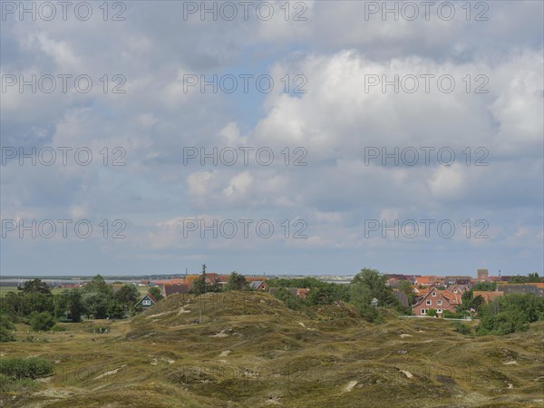 A hilly landscape with vegetation and houses in the background under a cloudy sky, Baltrum Germany