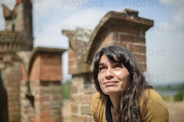 Thoughtful latino young woman sits on an old brick wall, casually dressed, enjoying a peaceful