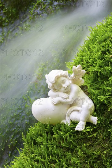 Porcelain angel figurine on moss by a waterfall