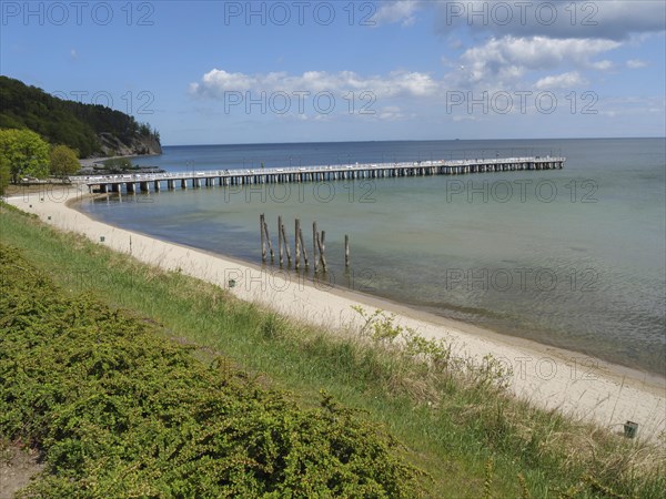 A sandy beach with a jetty leading into the sea, green coast and cloudy sky in the background,