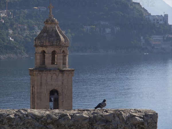 A bell tower with a dove in the foreground, the sea and mountains in the background, a peaceful