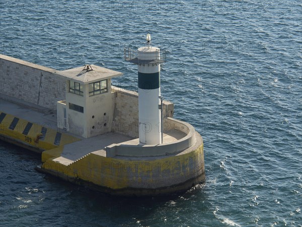 A lighthouse at a harbour surrounded by blue water in daylight, Ancient buildings with columns and
