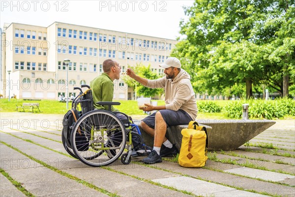 Full length photo of a caucasian adult college student feeding a friend with cerebral palsy on