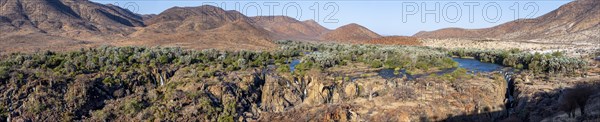 Panorama, Kunene River with green vegetation in dry red mountain landscape, waterfall and African
