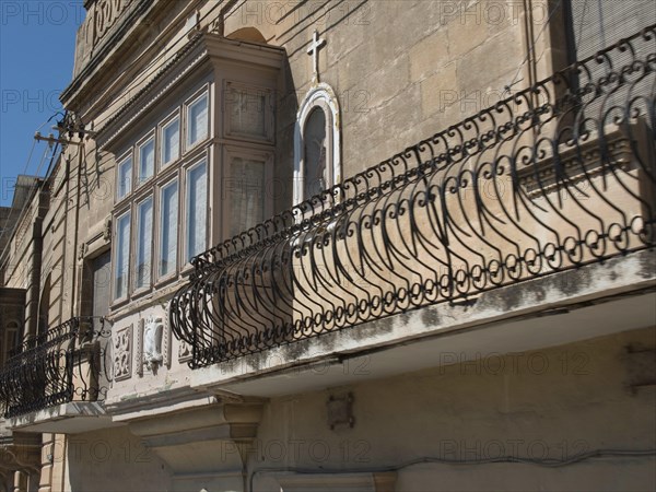 Facade of an old building with wrought iron balcony railings and a cross on a niche, the island of