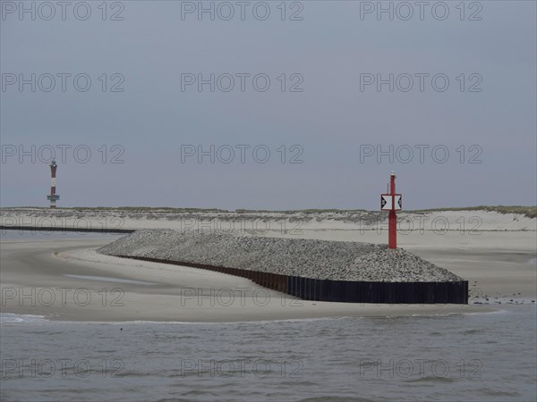 Red beacon on a gravel embankment along the coast with sand dunes and grey sky, buhne on an island